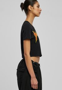 Tricou scurt negru din bumbac, cu un design grafic galben și roșu. Are mâneci scurte și guler rotund. Se potrivește cu pantaloni negri.