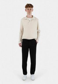 Crèmefärgad stickad tröja med krage, tillsammans med svarta byxor och vita sneakers. Enkelt designad med en avslappnad passform.
