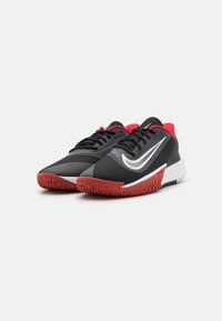 Černé sportovní boty s červenými akcenty, s texturovaným svrškem, bílým logem swoosh a vzorovanou červenou gumovou podrážkou.