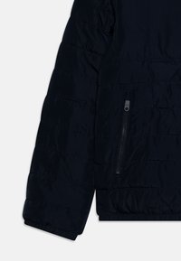Marineblaue Steppjacke mit gepolstertem Design, wattierter Textur und einer Reißverschlusstasche am linken Ärmel. Die Bündchen sind elastisch für eine optimale Passform.
