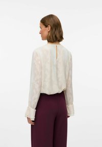 Kreemikleit lillemustriga pluus, millel on läbipaistev tekstuur ja pikad varrukad. Omab avatud seljaosa ning pehmeid laiu mansette. Ühendatud burgundia värvi pükstega.