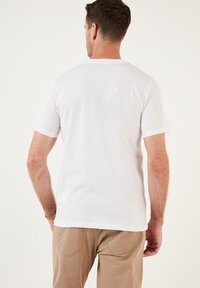 T-shirt bianca a maniche corte realizzata in cotone, con collo rotondo e una texture liscia, mostrata dal retro con dettagli minimi.