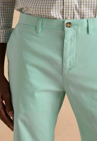 Világos menta zöld nadrág sima textúrával, elülső gombos zárral, övhurkokkal és oldalzsebekkel.
