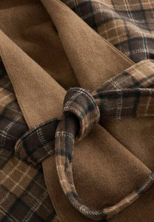 Brun ulltyg med en slät textur, som har ett mörkt rutmönster, knutet med ett matchande bälte, vilket skapar en lager-på-lager-look.