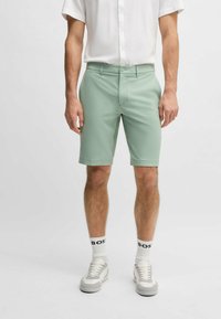Mint green shorts with a flat front and belt loops, tailored fit, worn with a white short-sleeve button-up and sneakers.