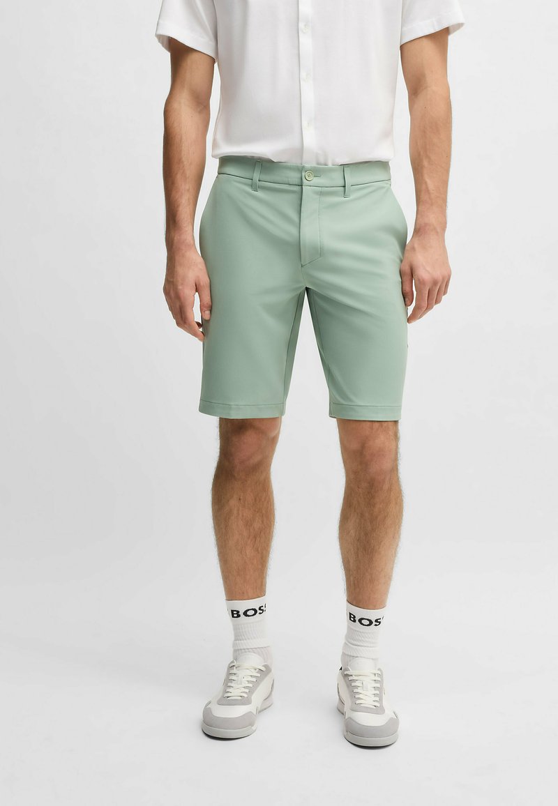 Mint green shorts with a flat front and belt loops, tailored fit, worn with a white short-sleeve button-up and sneakers.