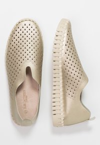 Zapatos dorados tipo slip-on con un diseño texturizado y con ondulados. Suela flexible con estrías, que presenta una puntera abierta y un interior suave.