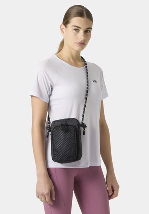 Kobieta ubrana w biały krótki rękaw i różowe leginsy, z czarną teksturowaną torebką na ramię zawieszoną na ramieniu.