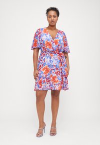 Cvečni zavojni plašč z dolgimi, rahlo letečimi rokavi. Ima barvit vzorec oranžnih in modrih cvetov na svetlem ozadju. Vključuje tkaninsko zavezo.