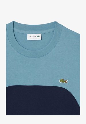 Camiseta de manga corta con una sección superior de color azul claro y una parte inferior de color azul marino, hecha de una tela suave con un logo de cocodrilo bordado.