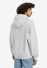 Grå sweatshirt med en rummelig pasform, blød tekstur, justerbar hætte og ribbede manchetter, parret med lyseblå denimjeans.