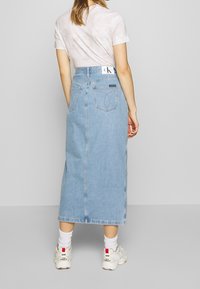 Světle modrá džínová maxi sukně s vysokým pasem, zadními kapsami a viditelným středovým švem, kombinovaná s bílými teniskami a krátkými ponožkami.