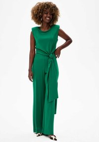 Groene jumpsuit met brede benen en een geknoopte riemdetail rond de taille. Glad, glanzend materiaal met mouwloos ontwerp en schoudervullingen.