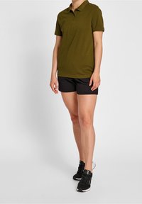 Olivově zelená polokošile s krátkým rukávem, doplněná černými sportovními šortkami a černými teniskami s bílými akcenty. Jednoduchý design.