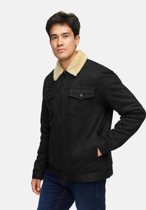 Chaqueta de ante negra con un cuello de piel sintética beige, presenta un cierre frontal de cremallera, dos bolsillos en el pecho y bolsillos laterales. Textura suave, diseño casual.