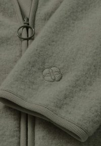 Fleecejacke in gedämpftem Grün mit glatter Textur, gerippten Bündchen und einem runden bestickten Logo am Ärmel. Reißverschlussdetails.