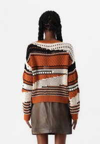 Neulottu pusero, jossa oransseja, mustia ja kermaisia raitoja; avoin pitsikuvio; resorit hihansuissa ja helmassa. Yhdistetty tumman nahkahameen kanssa.