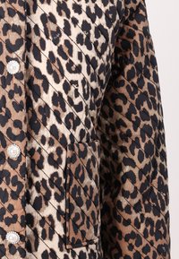 Chaqueta acolchada con estampado de leopardo en negro y beis, dos grandes botones similares a perlas y un bolsillo diagonal en la parte delantera.