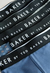 Dvi poros vyrų šortukų, kurie išdėstyti, turi tamsius elastingus dirželius su „BAKER BY TED BAKER“ baltomis raidėmis ir mėlyną audinį su apvalių raštų motyvu.