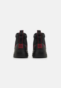 Zapatillas altas negras con acentos rojos, con parte superior de tela texturizada, suela de goma y detalle de marca en el talón.