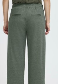 Pantaloni largi, verzi, cu textură moale, având talie elastică și două buzunare la spate. Ton neutru, potrivit pentru ținute casual.