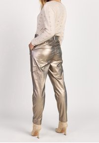 Pantaloni metallici dorati con una vestibilità morbida, dotati di una tasca laterale e di un elastico in vita leggermente elastico, abbinati a un maglione di maglia beige.