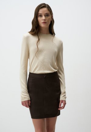 Un haut en tricot beige à manches longues associé à une minijupe marron ajustée. Le haut présente une texture côtelée et la jupe a des poches à l'avant.