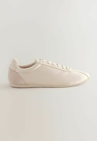 Beige low-top sneakers with a smooth leather upper, suede heel accent, and six eyelets for laces, featuring a rounded toe design.