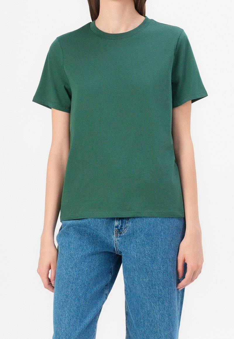 T-shirt en coton vert à manches courtes, col rond, texture lisse et coupe décontractée, associé à un jean en denim bleu.