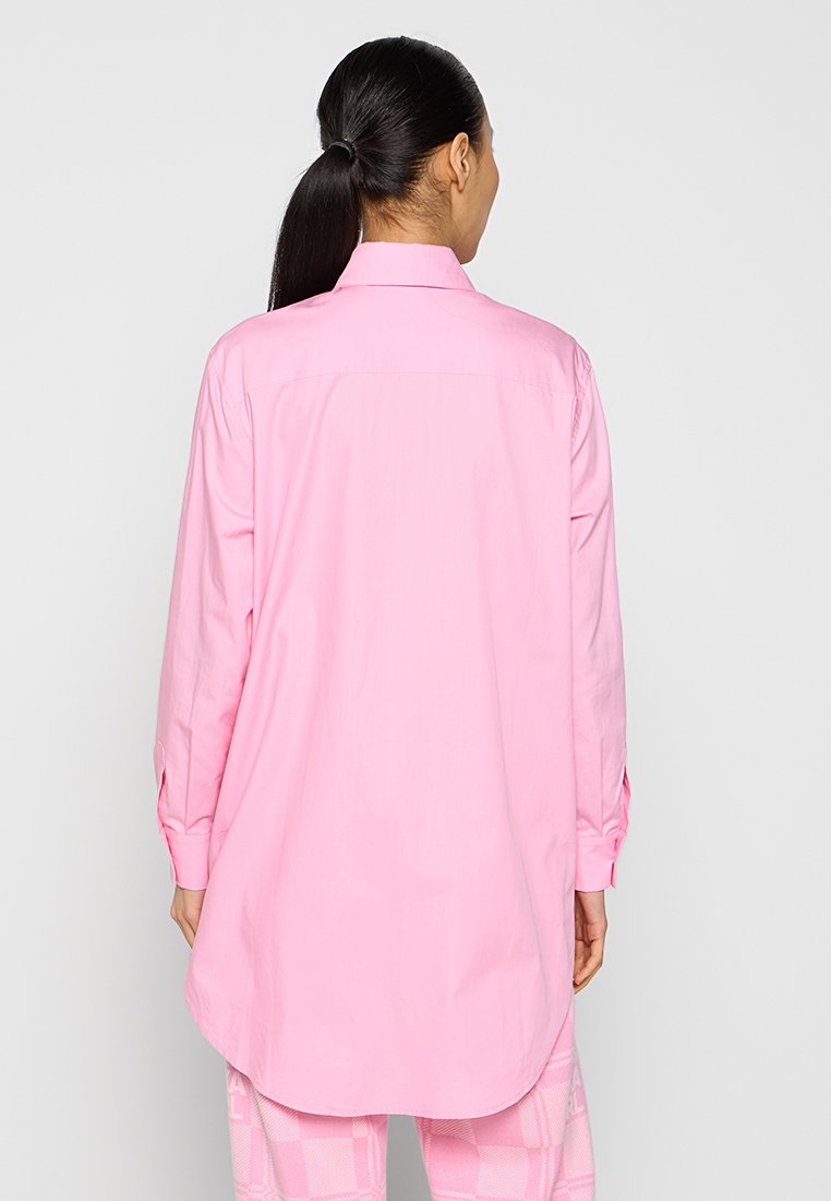 Chemise à manches longues de couleur rose vif, en coton lisse, avec un col pointu, des poignets boutonnés et un ourlet arrondi au dos.