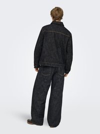 Donker denim jack en broek, met een relaxte pasvorm, zichtbare stiksels en achterzakken. De stof heeft een gestructureerde afwerking met subtiele kleurvariaties.