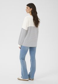 White and navy striped sweatshirt with long sleeves, blue flared jeans, and light shoes. Hair falls loosely past shoulders.