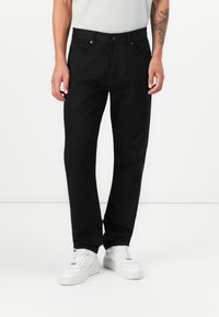 Black denim trousers with a straight cut, featuring a button closure, belt loops, and front and back pockets, worn with white sneakers.