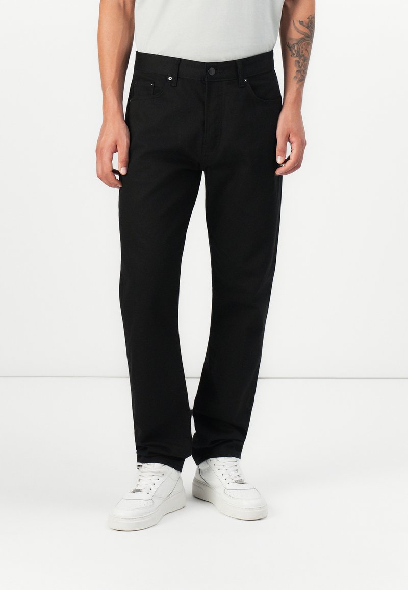 Black denim trousers with a straight cut, featuring a button closure, belt loops, and front and back pockets, worn with white sneakers.