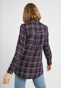 Chemise à carreaux marine avec motif grille rouge et blanc, à manches longues et ourlet arrondi. Fabriquée en tissu léger avec une coupe décontractée.