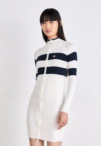 Abito in maglia a coste bianco con righe orizzontali blu navy, chiusura frontale con zip a tutta lunghezza, maniche lunghe e piccolo logo sul petto.