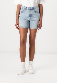 Ljusblå denimshorts med hög midja, klassisk femficksdesign, fransad fåll och blixtlås med knappstängning. Kombineras med vita sneakers.