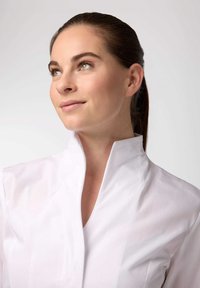 Camicia bianca con colletto alto, realizzata in tessuto liscio. Il design presenta linee pulite e una silhouette aderente.