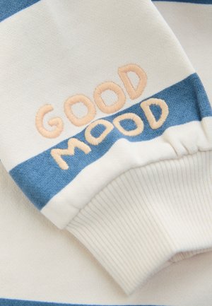 Poignet de sweat-shirt en tissu rayé crème et bleu avec un texte brodé "GOOD MOOD" en fil pêche. Texture douce, coupe décontractée.