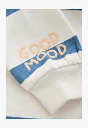 Manžeta od pulovera s kremasto-plavim prugastim tkanjem, ukrašena izvezenim tekstom "GOOD MOOD" u breskvastoj boji. Mekana tekstura, ležerni kroj.