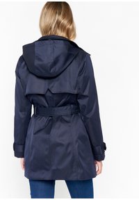 Mörkblå regnkappa med huva, bälte vid midjan och innefickor i ryggen; tillverkad av ett slätt, vattenavvisande material med knäppningar vid ärmsluten.