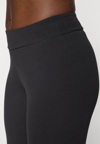 Fekete, magas derekú leggings rugalmas anyagból, sima textúrával és testhez simuló kialakítással, amely követi a test vonalát.