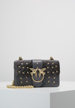 Ciemnoszara pikowana torebka z złotymi ćwiekami w kształcie ptaków, złotym zapięciem w formie pierścienia w kształcie ptaka oraz złotym łańcuszkiem na białym tle.