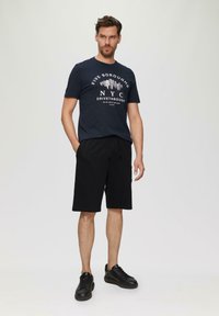Marineblauwe katoenen t-shirt met witte "Five Boroughs NYC Drive Through" grafiek, gecombineerd met zwarte shorts met trekkoord en zwarte sneakers.