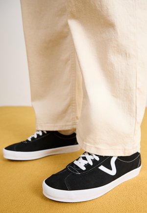 Sorte semskede sneakers med hvite detaljer og snøring, med lavt design og rund tå, brukt med beige vide bukser.