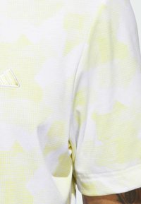 Short sleeve t-shirt in white and light yellow, featuring a dotted pattern and a small embroidered logo on the chest.