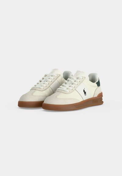 Ζευγάρι λευκά low-top αθλητικά παπούτσια με καφέ λαστιχένιες σόλες, κλείσιμο με κορδόνια και μικρό μαύρο λογότυπο Polo στο πλάι με πράσινες λεπτομέρειες στη φτέρνα.