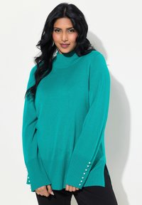 Türkise Pullover mit hochgeschlossenem Kragen, gerippten Bündchen und seitlichen Schlitzen. Mit Perlenakzenten an den Ärmeln. Hergestellt aus einem weichen Material.