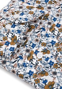 Koszula w kwiaty z białej tkaniny, zdobiona niebieskimi, brązowymi i czarnymi kwiatami z zielonymi liśćmi; zawiera białe guziki i złożony kołnierzyk.