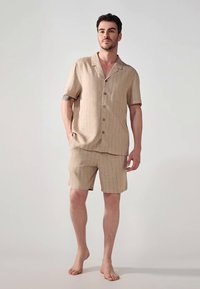 Beige kortermet skjorte og matchende shorts-sett, med et subtilt rutemønster, knappestolpe foran og en avslappet passform med sidelommer.